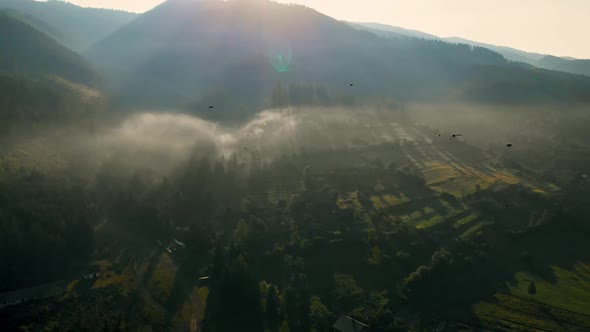 Aerial view of sunrise over foggy village in mountains.