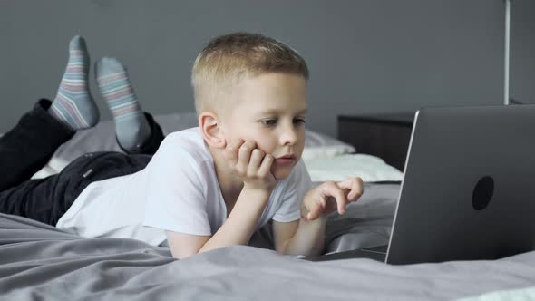 The Child Looks at The Screen, Uses a Laptop, Plays Games at the Computer. The Boy is lying alt