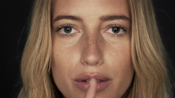 Woman holding finger to lips, close-up alt