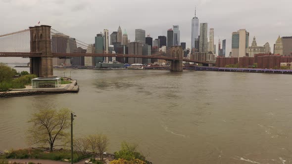 An aerial view over the East River on a cloudy day. The drone camera dolly out from the Brooklyn Bri alt