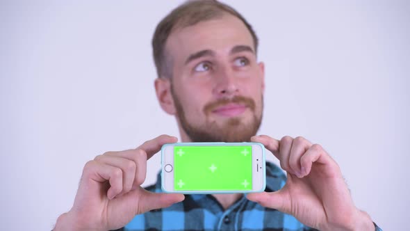 Face of Happy Bearded Hipster Man Thinking While Showing Phone alt