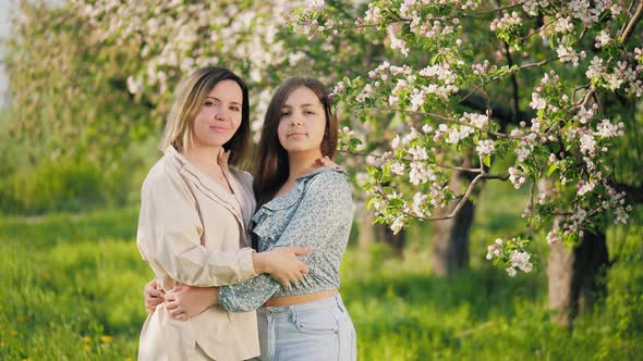 Portrait of a Woman with Her Teenage Daughter Standing in a Blooming Garden alt