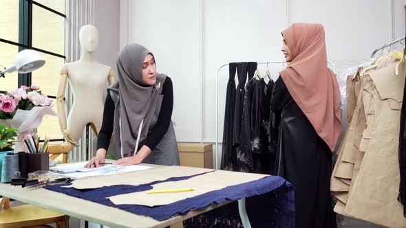 Muslim woman fashion designer working in tailor shop with her assistant