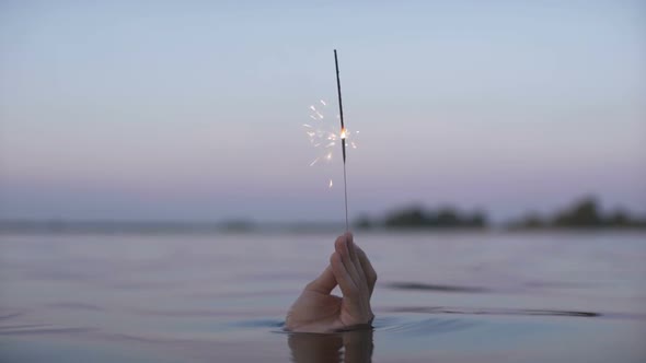 Man's Hand From the Water Holding a Sparkler