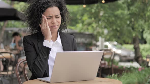 African Woman with Headache Using Laptop in Outdoor Cafe alt