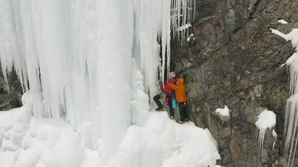 Ice climbers prepare to climb cascade breaking icicles 4K alt
