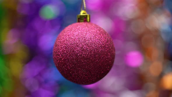 Spinning red Christmas ball on blurry bokeh background of colored and glowing tinsel, holiday lights