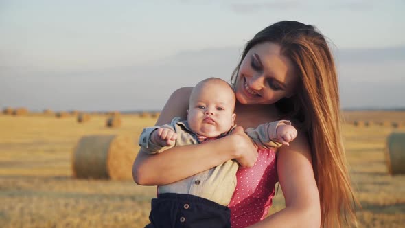 Portrait of a Little Baby Son in Mother Hands is Caressed in Spacious Hay Field alt
