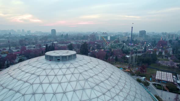 Aerial view dolly in of the ellipse and amusement park at O'Higgins Park, Santiago, Chile. Sunset wi alt