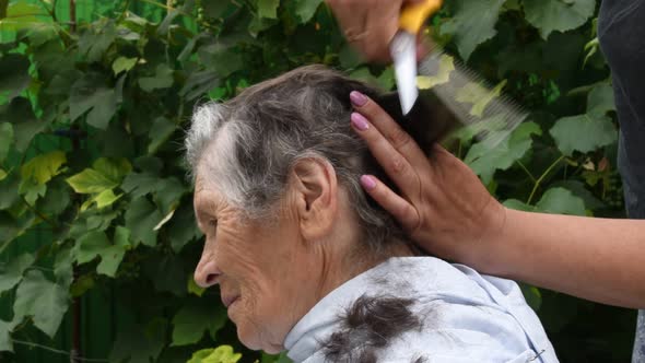 Female Hands Hold Scissors and Cut 80s Senior Woman Hair at Backyard