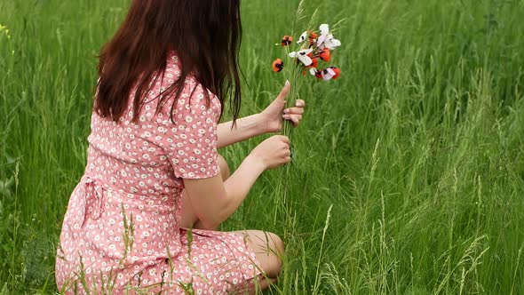 A woman in a beautiful dress collects a spring bouquet of flowers in a field with green grass. alt
