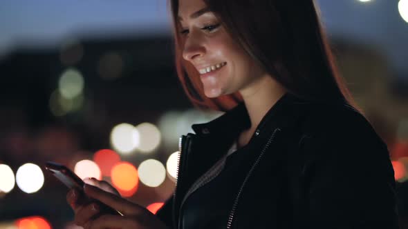  young Smiling Woman Holding Smartphone, and Looking at It