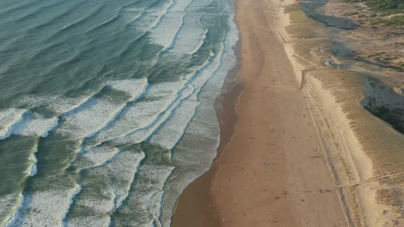 Few People on Wide Brown Beach Keeping Distance at Beautiful Golden Hour with White Green Waves alt
