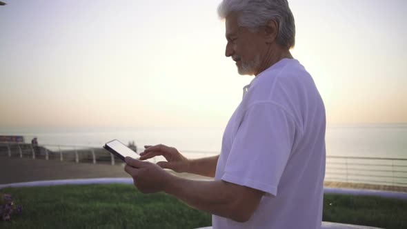 Portrait of Retirement Handsome Senior Man Using Tablet Computer on Seafront alt