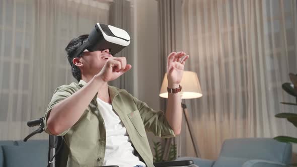 Funny Asian Man Sitting In A Wheelchair While Wearing Virtual Reality Goggles At Home alt