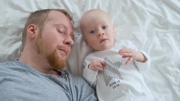 baby in a bodysuit with the inscription born in 2019 lies next to a sleeping dad