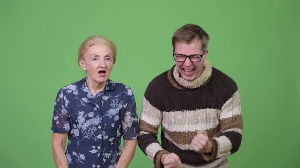 Grandson Celebrating While Grandmother Looking Upset Against Green Background alt