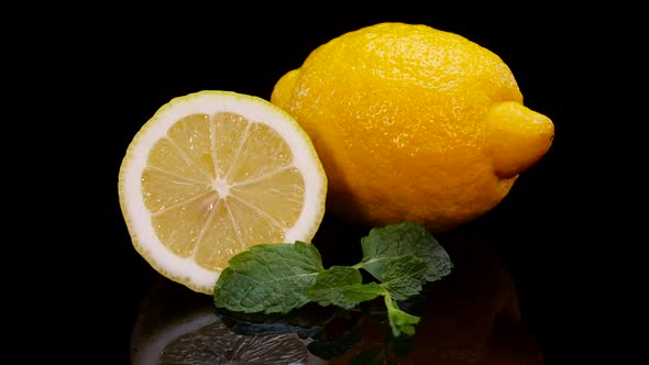 Yellow lemon with mint leaves rotating on a black background.