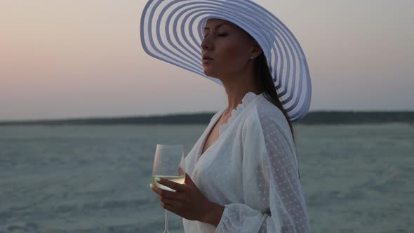 Elegant Woman with Glass of Wine Resting on Beach at Sunset