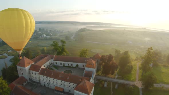 Colorful Hot Air Balloons Fly Over the Medieval Castle and Lake in the Morning Fog. Maneuverable alt