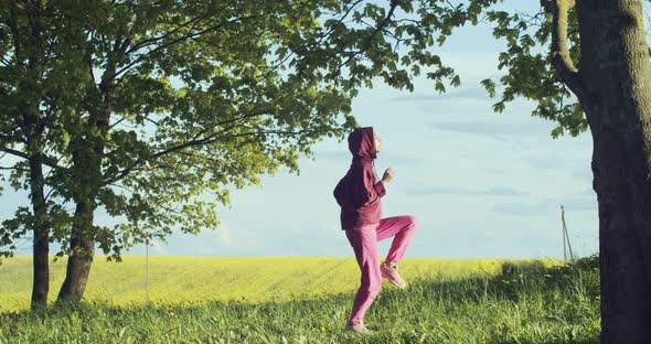 Side View of Female Athlete in Pink Sportswear Running in Place Outdoors on Wild Nature. Young Woman