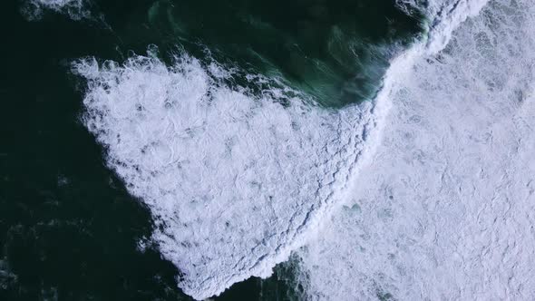 Massive Atlantic swells crash onto coastline, whitewash in shallows; aerial alt