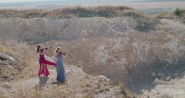Violinists in Blowing Dresses Play Music Among the Picturesque Cliffs in Summer alt