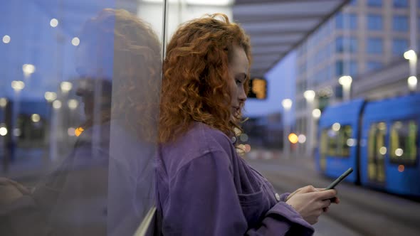 Pretty woman leaning on glass pane at train station using smartphone