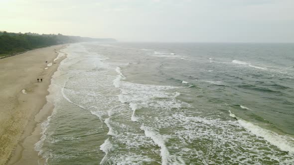 Sun Shines over the Horizon in the Evening as a Couple takes a Walk on a Freezing Cold Beach, Drone alt