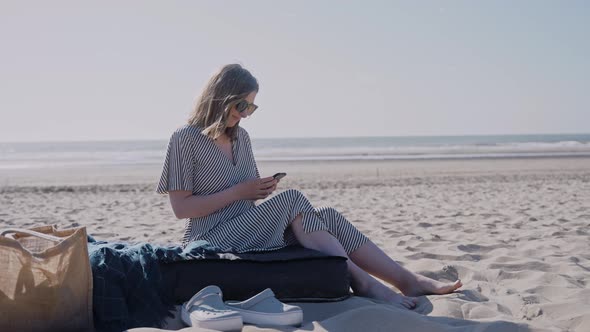 A Woman Sits on an Ocean Beach and Looks at Her Phone