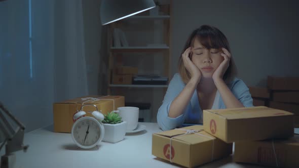 Young Asian business woman owner of SME sleepy exhausted working at office desk in night at home. alt