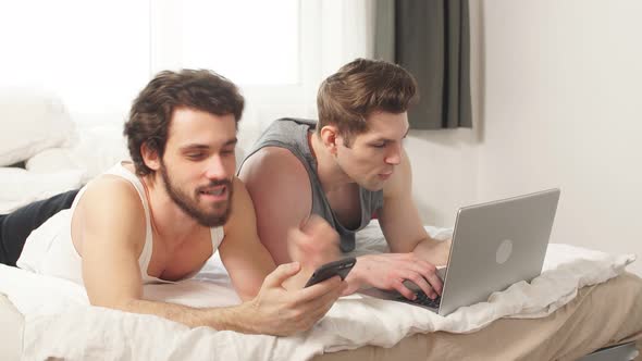 Cute Male Gay Couple Spend Time at Home. They Are Sitting Down on a Sofa and Use the Laptop. alt