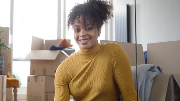 Portrait Of Young Woman Sitting On Floor And Smiling As She Moves Into New Home Surrounded By Boxes