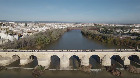 Fly over Roman Bridge of Córdoba, Guadalquivir River on a sunny day, Spain