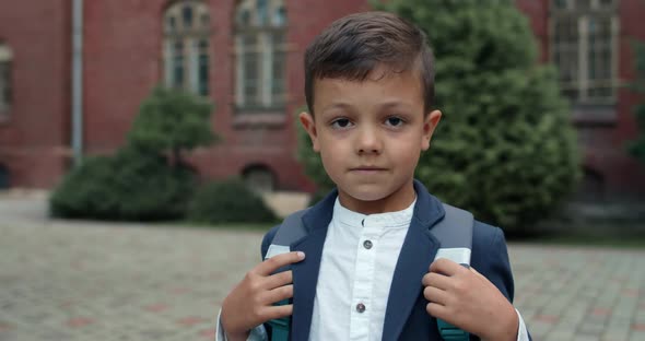 Close Up View of Little Kid with Bag Looking To Camera. Cute Boy in School Uniform Posing While alt