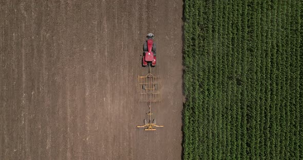 Red tractor flattening a field for seeding, Drone follow footage. alt