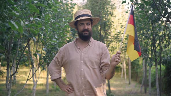 Positive German Bearded Gardener with Mustache in Straw Hat Posing Outdoors with National Flag on alt