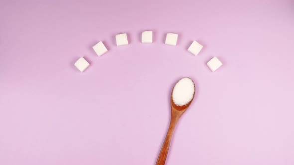 Diabetic blood sugar scale made of white sugar cubes and wooden eco spoon rolls over pink background