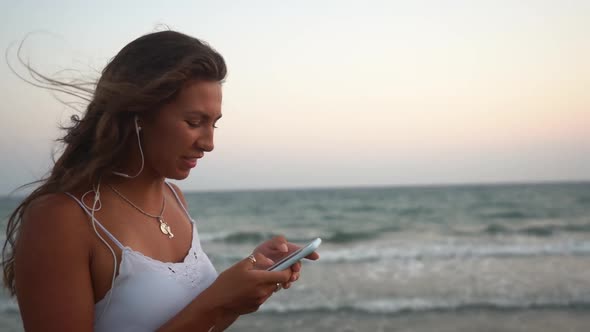 Young Woman with Earphones Using Smartphone on Beach in Summer