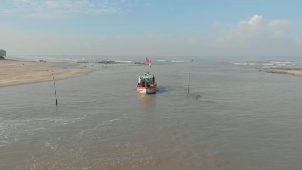 Drone shot of small colourful Indian fishing boat leaving a beach dock alt