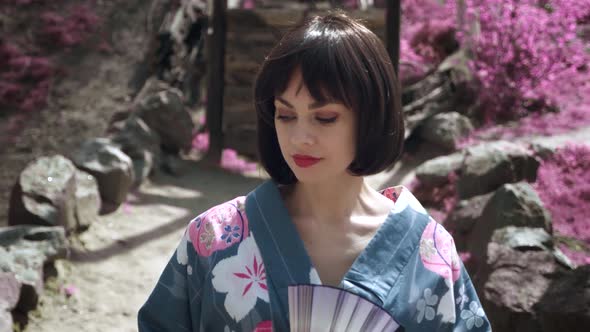 Portrait of Caucasian Woman Dressed Like Japanese Geisha Standing Outdoors on Sakura Trees alt