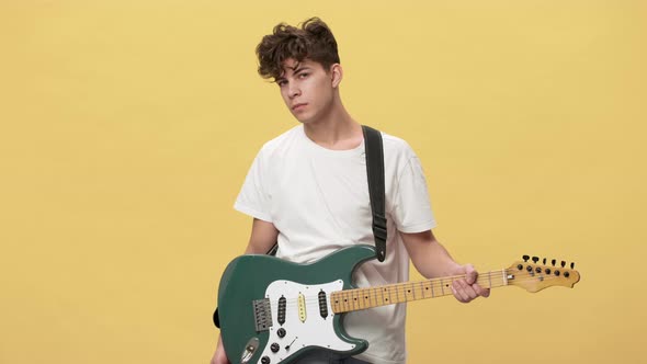 Portrait of Teenage Boy with Short Curly Hair Posing with Electric Guitar on Stage Over Yellow alt