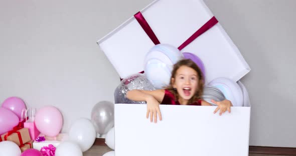 Cute, joyful little girl in pink dress jump out of the big present gift box with balloons  alt