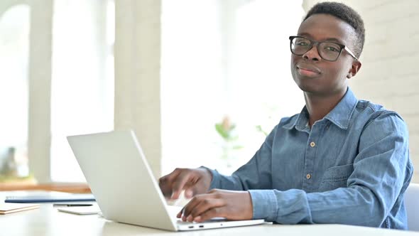 Young African Man with Laptop Pointing with Finger at Camera alt