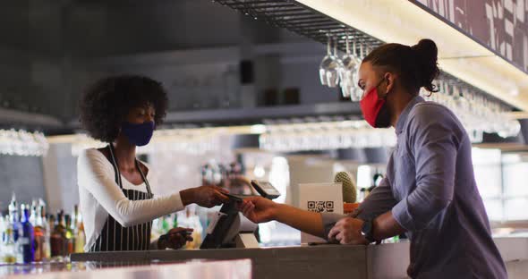 Mixed race man giving african american female cafe worker his credit card in order to pay alt
