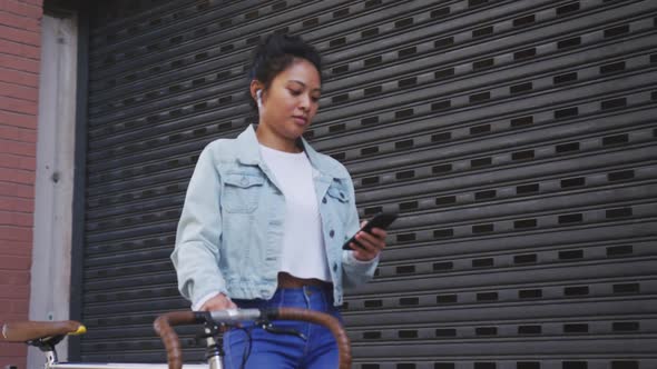 Mixed race woman walking next to her bike on the street alt
