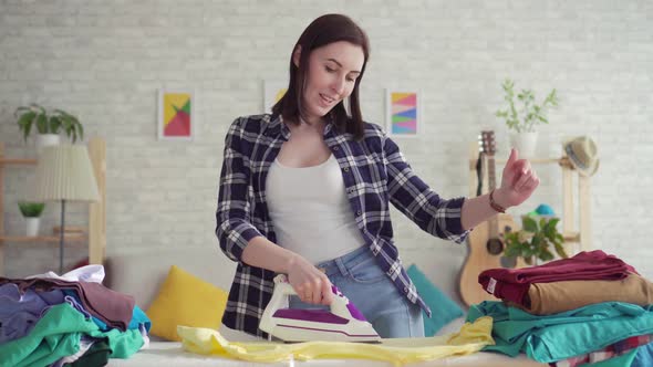 Cheerful Young Woman in Plaid Shirt Ironed Linen Iron at Home Dancing alt