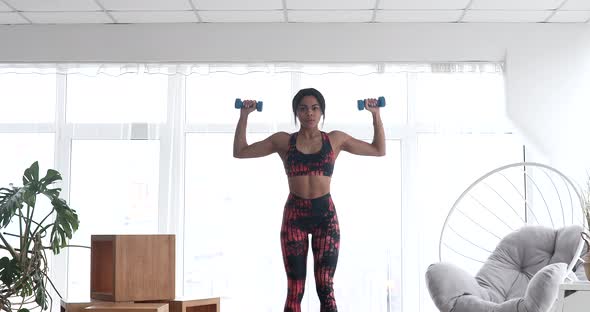 Fit black woman doing fitness at home with dumbbells.