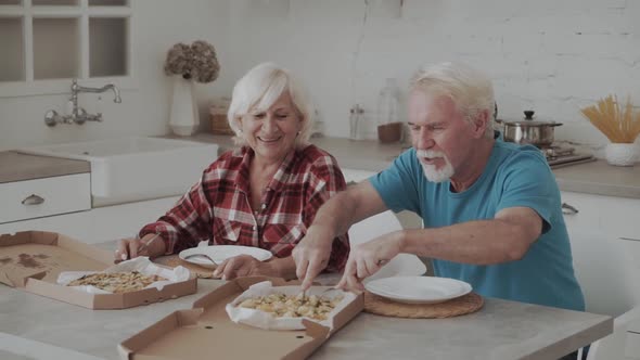 Senior Couple Sharing Takeaway Pizza In Kitchen alt