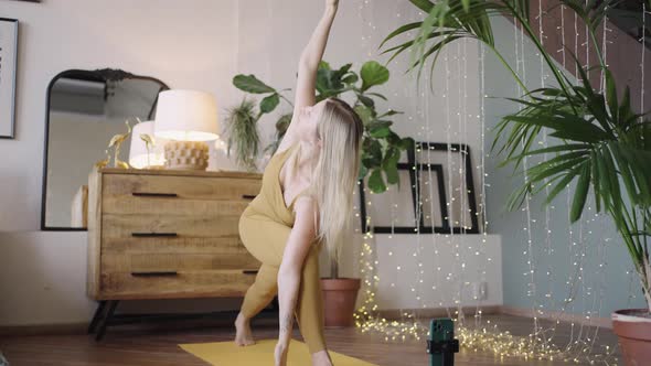 Young Woman Does Yoga Talking Via Videocall Using Phone alt